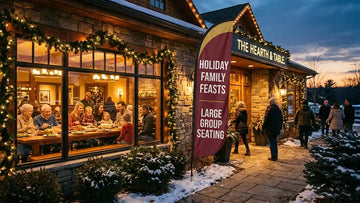 Warm restaurant storefront with Holiday Family Feasts Large Group Seating feather flag welcoming arriving families