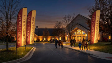 Thanksgiving Eve twilight communion church feather flags warmly illuminated along driveway
