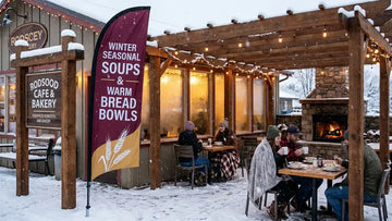Cozy roadside cafe patio with 13ft Winter Seasonal Soups & Warm Bread Bowls feather flag fluttering in snow