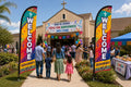 Two Hispanic / Bilingual Ministry church feather flags flanking main entrance with greeters and families arriving