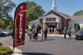 Classic Sunday Service church feather flag at parking lot entrance guiding first-time visitors