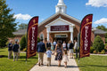 Two Classic Sunday Service church feather flags flanking main entrance with greeters and families arriving