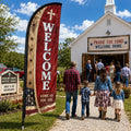 Rustic red country church feather flag with WELCOME text outside a rural church with families arriving