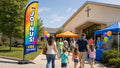 VBS Join Us church feather flag at family check-in entrance with parents and children arriving