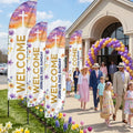 Four church Welcome feather flags lining an Easter Sunday walkway corridor with balloon arch and spring tulips — families walking through