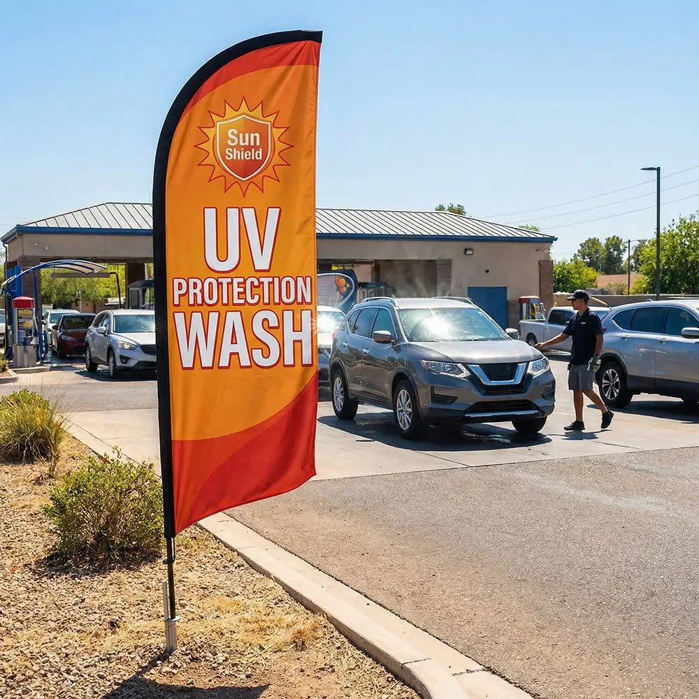 Vibrant UV Protection feather flag with sun icons standing at a car wash during a bright, sunny summer day.