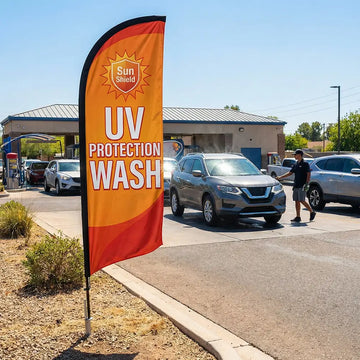 Vibrant UV Protection feather flag with sun icons standing at a car wash during a bright, sunny summer day.